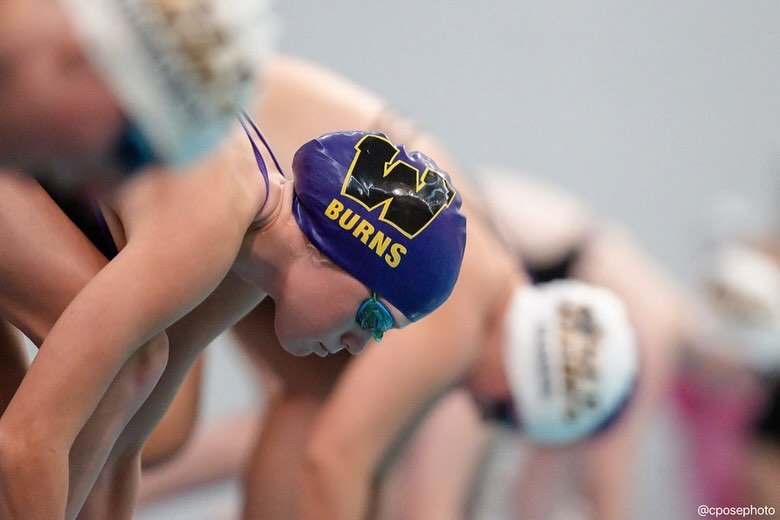 Waukee swimmer on the blocks in a purple W cap